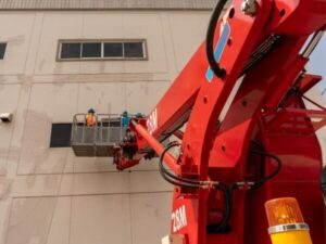 Autoscala con cestello rosso in uso per manutenzione su una parete industriale ad alta quota.